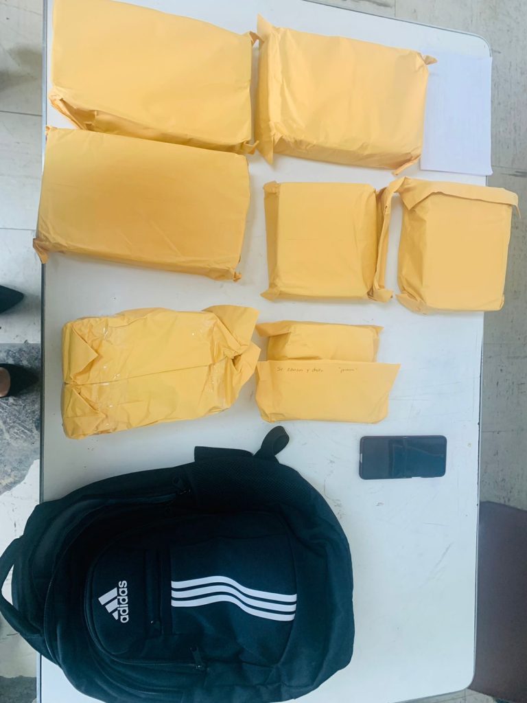 Nueve paquetes de color amarillo sobre una mesa y una mochila de color negro
