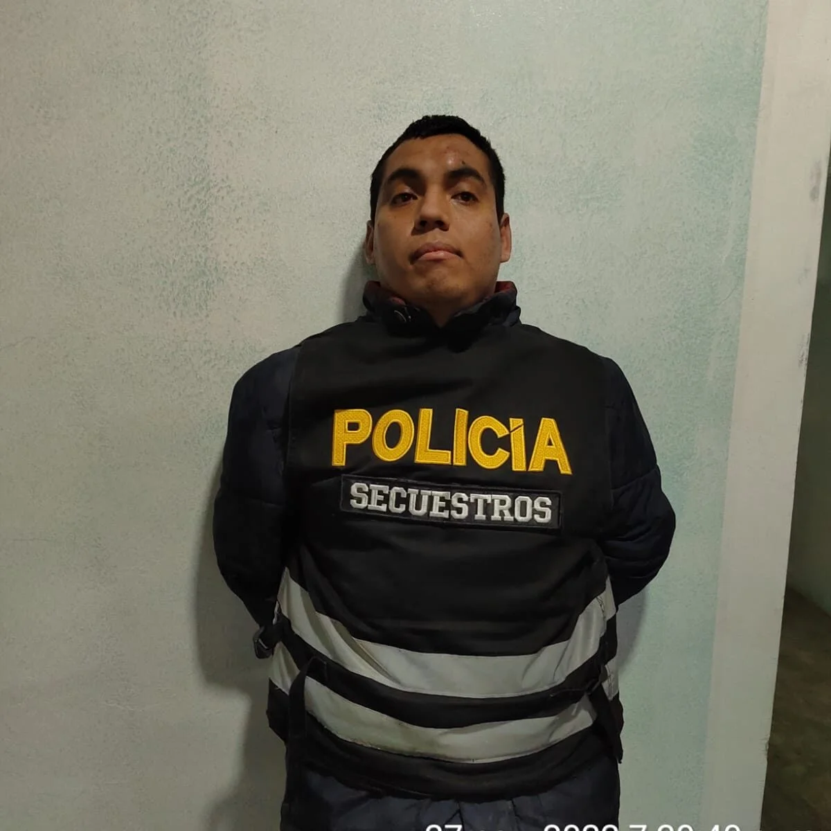 Presunto delincuente tiene los brazos en la espalda y luce chaleco de la policía