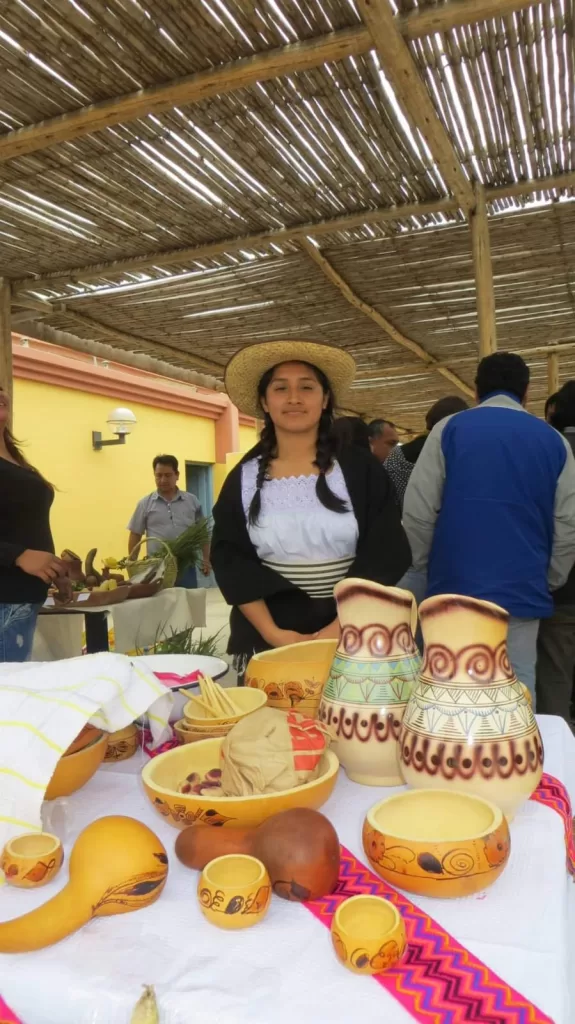 Una joven de la localidad de Moche mira a la cámara. Delante de ella, en una mesa se exhiben productos y la chicha de jora.