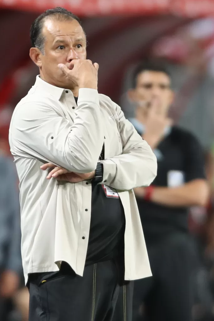 Reynoso analiza el partido en la zona técnica con la mano derecha en su rostro.